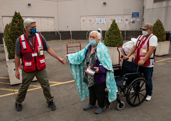 Kathie Tapia gets assistance from American Red Cross volunteers Rick Eilers, left, and Sivisay Rajsavong, right, as she returns home after staying at an American Red Cross shelter in Portland, OR on Monday, September 14, 2020. Ms. Tapia was evacuated from her home due to the threat of wildfires, but the danger level has been downgraded for the area where she lives so she is returning home. She says she will keep her bags packed in case the fire threatens her home again in which case she will return to the American Red Cross shelter.