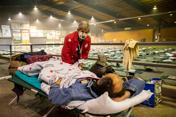 Patty Albin of the American Red Cross checks on Travis Wagner as he rests at the Jackson County Expo and Fairgrounds shelter after fleeing the wildfires in Central Point, OR on Sunday, September 13, 2020.