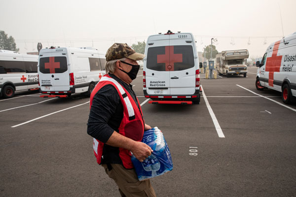 An American Red Cross volunteer carries bottled water to load into an Emergency Response Vehicle at a Red Cross command post and shelter in Salem, OR on Sept. 15, 2020. Photo by Scott Dalton/American Red Cross.