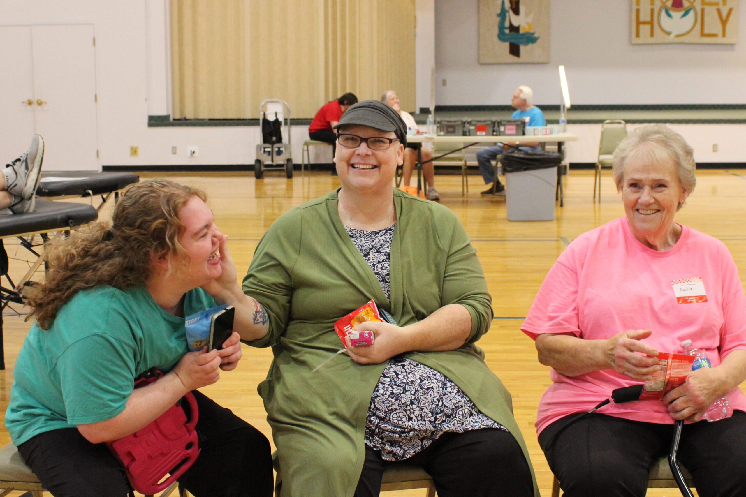 Mom sits at the blood donation site next to her daughter on the left and mother on the right. All are smiling.